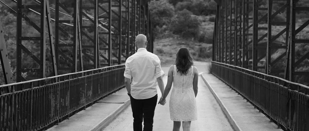 Laura et Florent marchent main dans la main sur un pont métallique, en noir et blanc