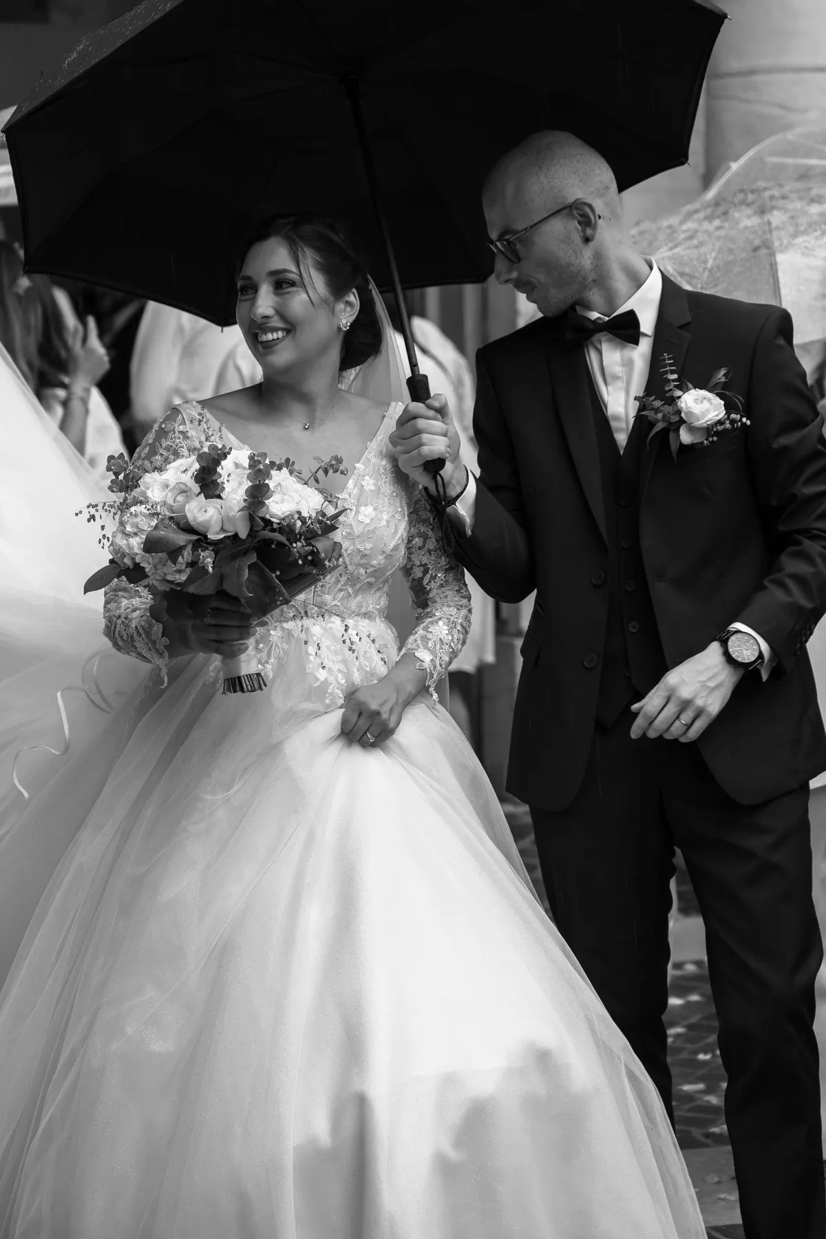 Les mariés souriants sous un parapluie à la sortie de la mairie, en noir et blanc