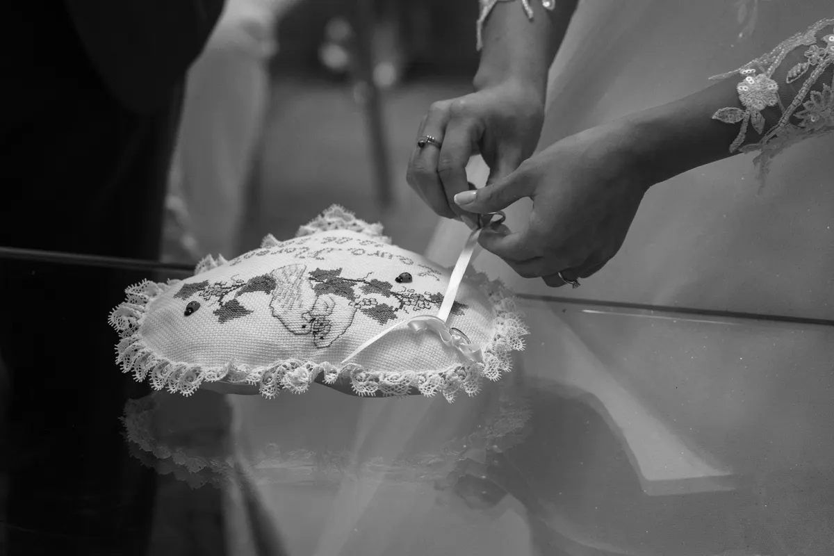 Mains déposant les alliances sur un coussin de dentelle, en noir et blanc