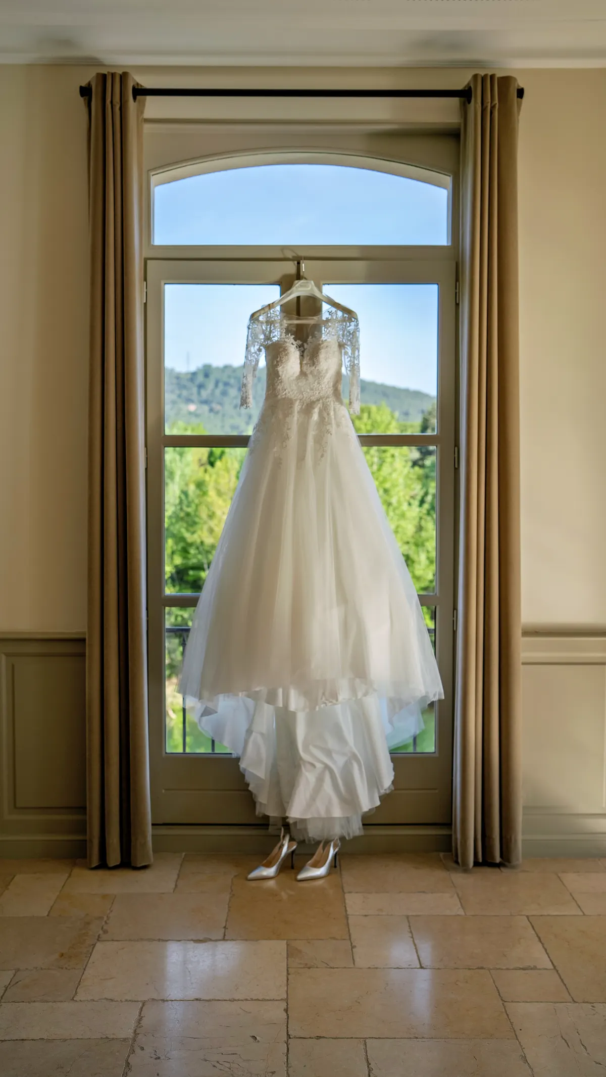 Robe de mariée suspendue devant une porte-fenêtre ouverte sur la verdure
